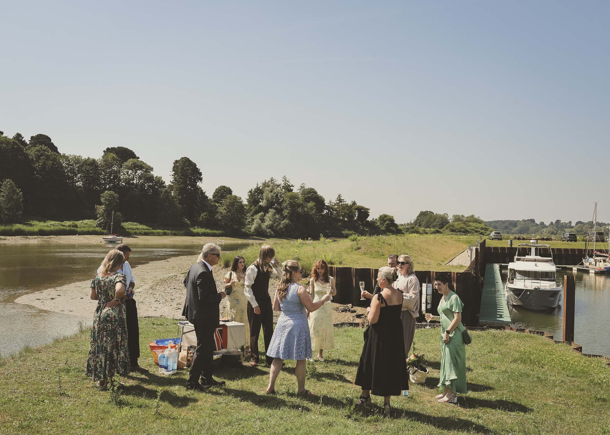 A bride and groom and their guests on the penisula at woodbridge marina on a wedding day in Woodbridge captured by Suffolk Wedding Photographer Hayley Denston Photography